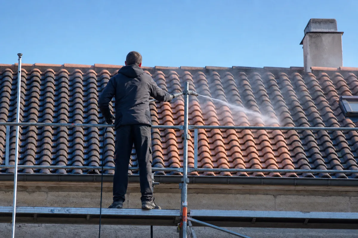 Couvreur nettoyant une toiture en tuiles à la lance basse pression depuis une nacelle