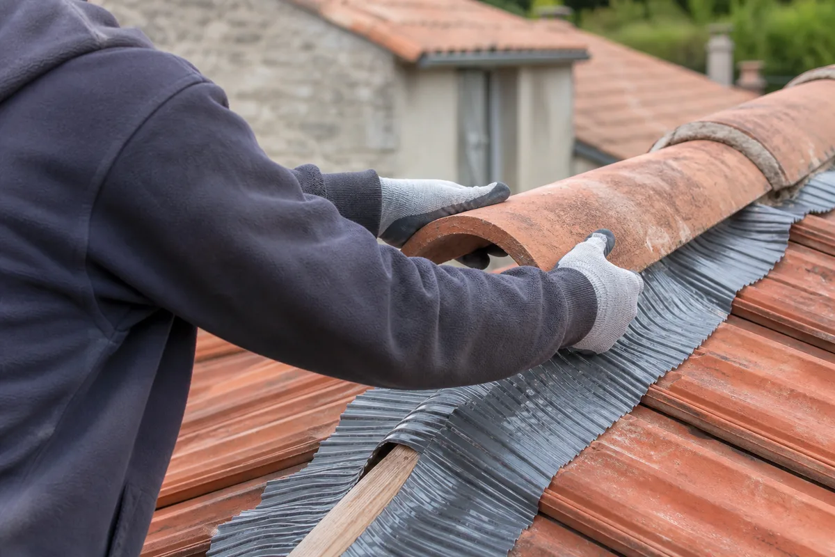 Couvreur posant une tuile faîtière sur un closoir ventilé au sommet d&rsquo;un toit en tuiles rouges