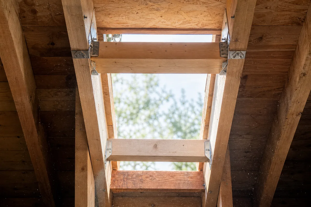Chevêtre en bois assemblé par sabots métalliques autour d’une réservation dans une charpente traditionnelle